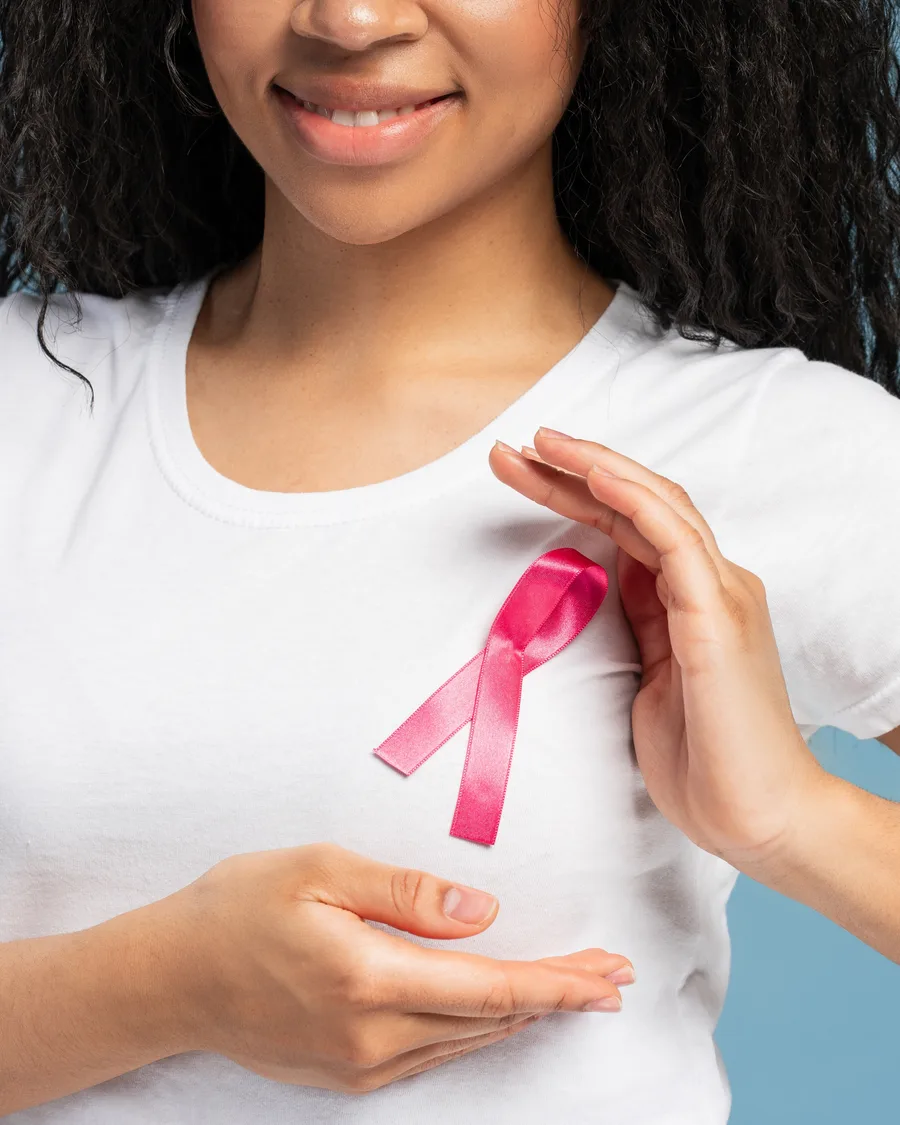 Mulher de camiseta branca com um laço rosa no peito, as mãos em volta da mama